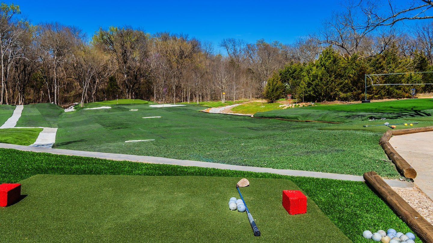Turf driving range with target greens, tee boxes and golf balls scattered across the grass