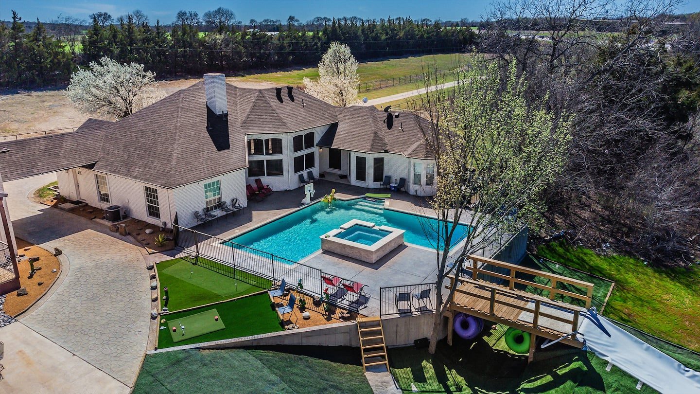 Aerial view of the main house with its fenced pool, hot tub and turf play areas